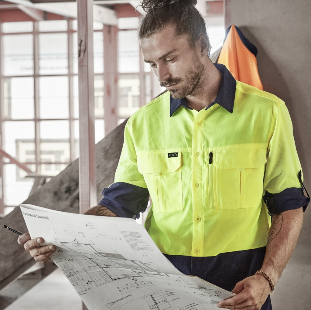 Image of a man wearing a high visibility shirt, looking at plans of a building.